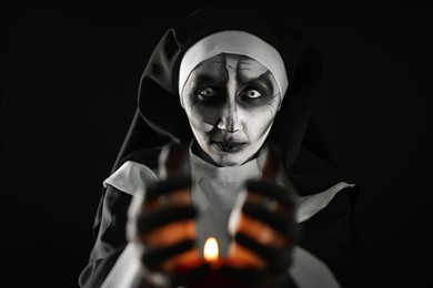 Scary devilish nun with burning candle on black background. Halloween party look