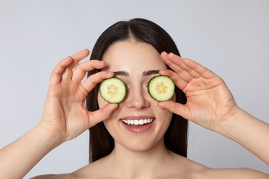Photo of Woman holding pieces of cucumber on light grey background. Spa treatment