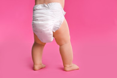 Back view of cute baby in dry soft diaper standing on pink background, closeup