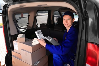 Photo of Courier with clipboard checking packages in delivery van