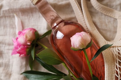 Photo of Rose wine and beautiful peonies in mesh bag on white fabric, closeup