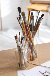 Holders with different paintbrushes on wooden table indoors. Artist's workplace