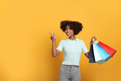 Photo of Smiling African American woman with shopping bags on orange background. Space for text