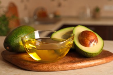 Photo of Fresh avocados and bowl of cooking oil on beige marble table in kitchen, closeup