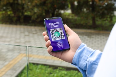 Photo of Man holding smartphone with activated promo code outdoors, closeup