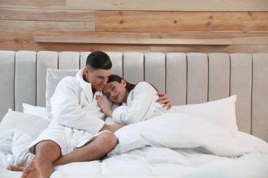 Happy couple in bathrobes resting on bed at home