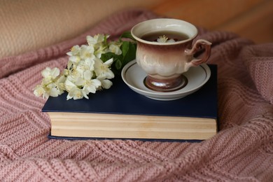Cup of aromatic tea with beautiful jasmine flowers and book on pink fabric