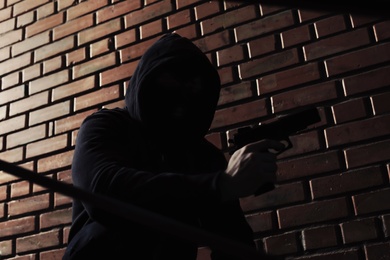 Man in hoodie with gun indoors. Dangerous criminal
