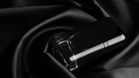 Luxury bottle of perfume on black silk, closeup