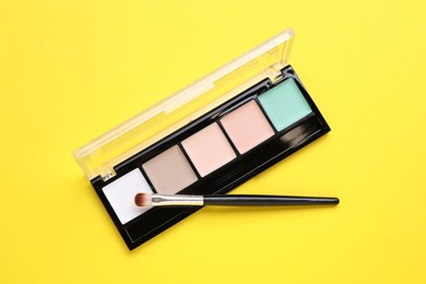 Photo of Colorful contouring palette with brush on yellow background, top view. Professional cosmetic product