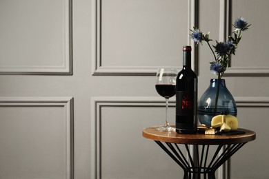 Bottle of red wine, glass, delicious snacks and beautiful bouquet on wooden table indoors. Space for text