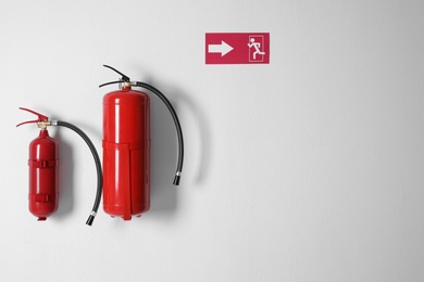 Different fire extinguishers and emergency exit sign on white wall. Space for text