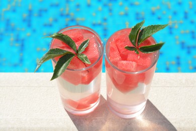 Refreshing watermelon drink in glasses near swimming pool outdoors