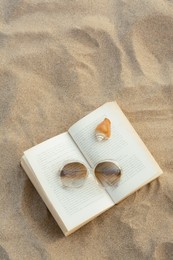 Photo of Beautiful sunglasses, book and shell on sand, top view. Space for text