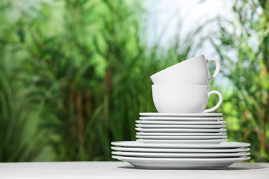 Photo of Set of clean plates and cups on white table against blurred background, space for text