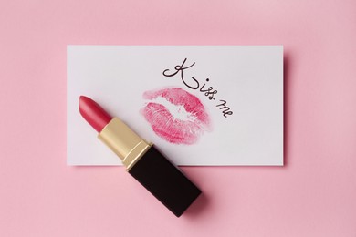 Paper card with lip print, phrase Kiss Me and lipstick on pink background, top view
