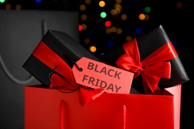 Paper shopping bags, gift boxes and tag with text Black friday against blurred lights, closeup