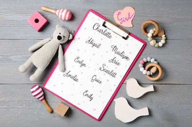Clipboard with different baby names and toys on grey wooden table, flat lay
