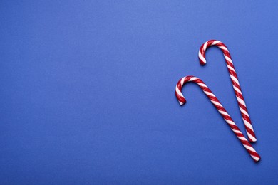 Two sweet Christmas candy canes on blue background, flat lay. Space for text