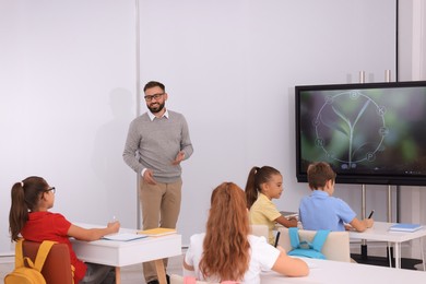 Teacher giving lesson to pupils near interactive board in classroom
