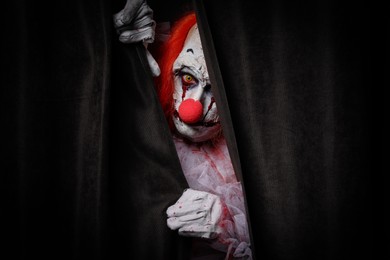 Terrifying clown hiding behind black curtains. Halloween party costume