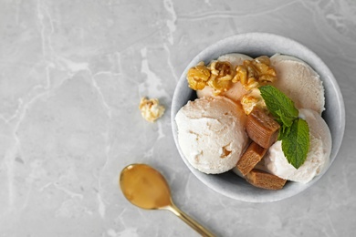 Bowl of delicious ice cream with caramel candies, popcorn and mint on light grey marble table, flat lay. Space for text