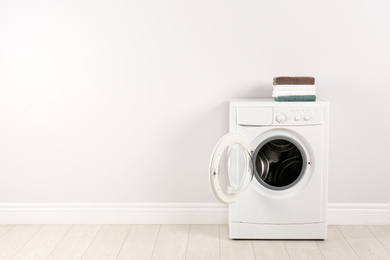 Modern washing machine with stack of towels near white wall, space for text. Laundry day