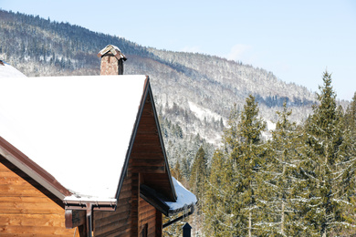 Wooden cottage covered with snow near conifer forest