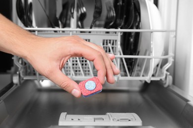Woman putting detergent tablet into open dishwasher in kitchen, closeup