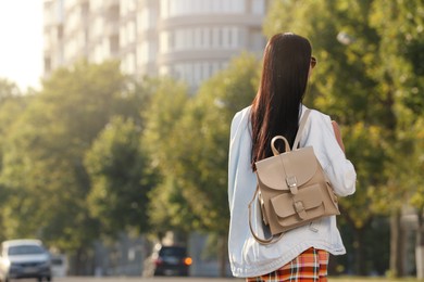 Photo of Young woman with stylish beige backpack on city street, back view. Space for text