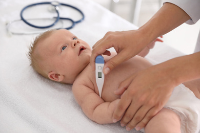 Doctor measuring temperature of little baby with digital thermometer indoors, closeup. Health care