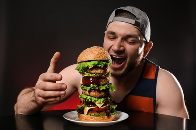 Photo of Young hungry man eating huge burger on black background