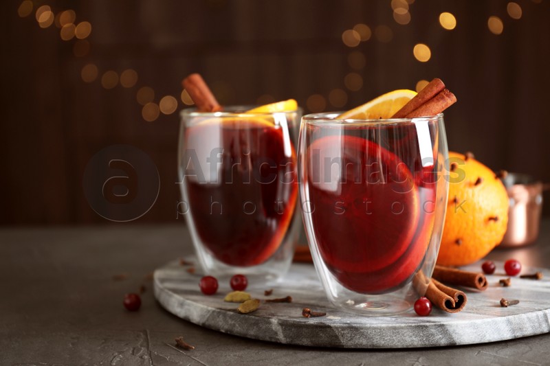 Glasses of tasty mulled wine on grey table against festive lights