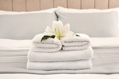 Stack of fresh towels with flower on bed indoors