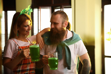Young woman and man with glasses of green beer in pub. St. Patrick's Day celebration