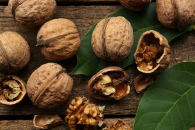 Whole and cracked walnuts with green leaves on wooden table, flat lay