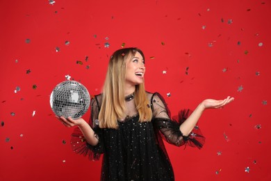 Happy young woman with disco ball and confetti on red background