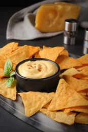 Photo of Delicious nachos and cheese sauce with basil on black table