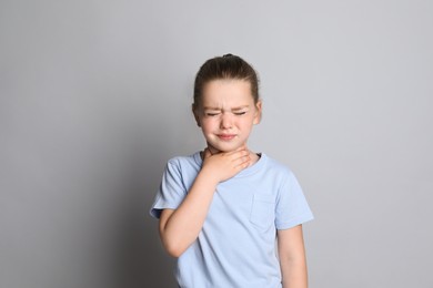 Little girl suffering from sore throat on grey background
