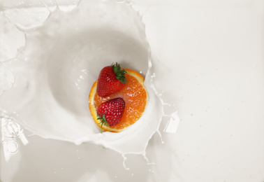 Slice of orange and strawberries falling in milk with splashes, top view