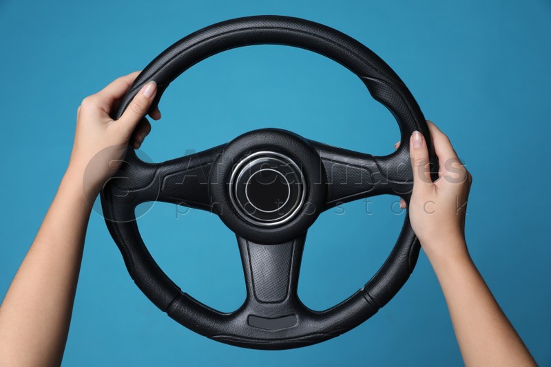 Woman holding steering wheel on blue background, closeup