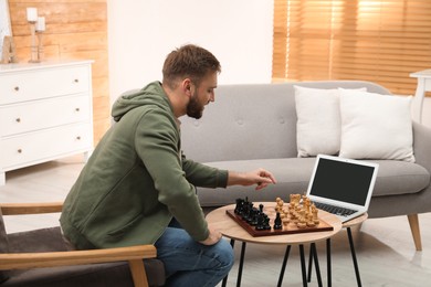 Photo of Young man playing chess with partner through online video chat in living room
