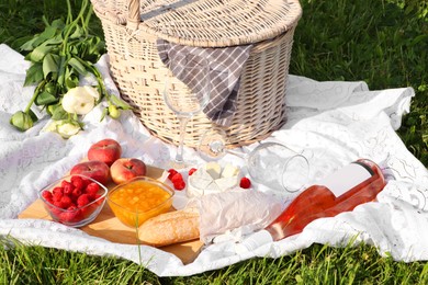 Photo of Picnic blanket with tasty food, flowers, basket and cider on green grass outdoors