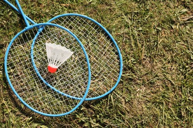 Badminton racquets and shuttlecock on green grass outdoors, flat lay. Space for text