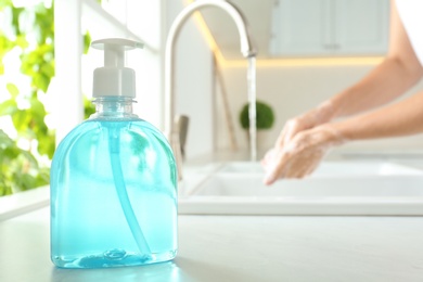 Bottle of antibacterial soap and blurred woman washing hands on background. Personal hygiene during COVID-19 pandemic