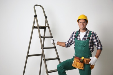 Professional builder near metal ladder on light background