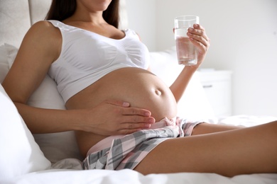 Young pregnant woman with glass of water in bedroom, closeup. Taking care of baby health