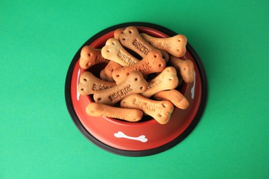 Photo of Bone shaped dog cookies in feeding bowl on green background, above view