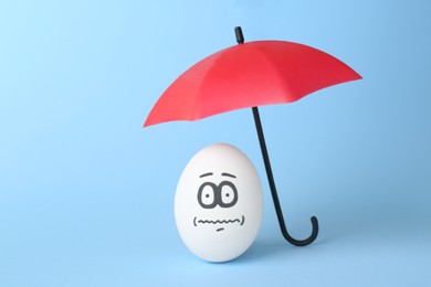 Egg with drawn frightened face and umbrella on turquoise background