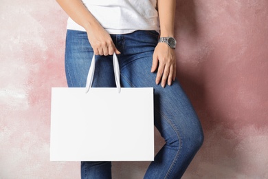 Woman holding mock-up of paper shopping bag on color background